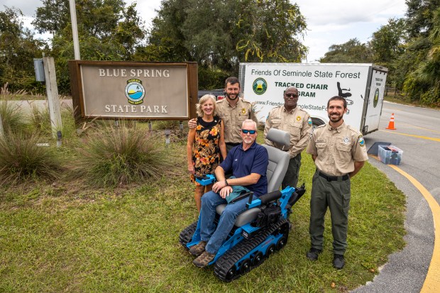 At the entrance of Blue Spring State Park in Orange City, from left, Katherine Hallum of Friends of Blue Spring, Dustin Allen, park manager, Greg Pauch of the Mesara Family Foundation, Darrell Thomas, assistant park manager, and Connor Wagner, park services specialist, gather to celebrate a new tracked chair program for visitors with mobility impairments on Oct. 26, 2023. The chairs can be reserved free of charge through an online system. (Patrick Connolly/Orlando Sentinel)